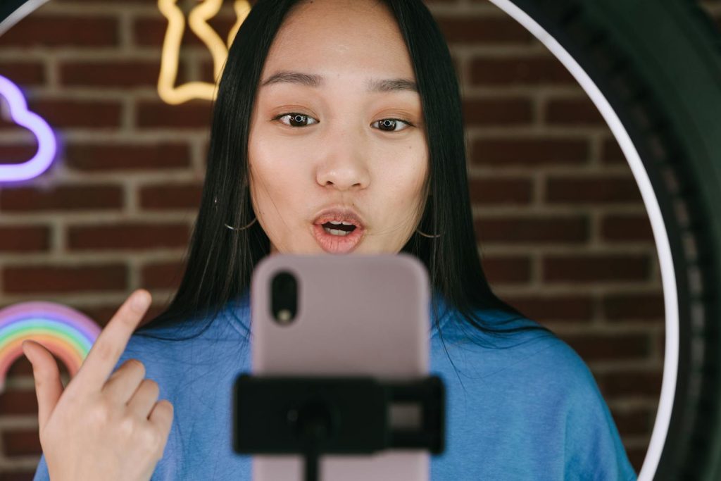 Asian woman vlogging with smartphone and ring light, in a creative indoor setting.